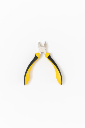 Open nippers with a bright yellow and black handle lying on a plain white background