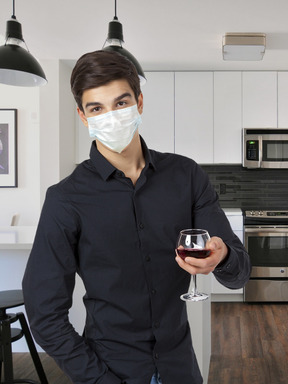 A man wearing a face mask holding a glass of wine