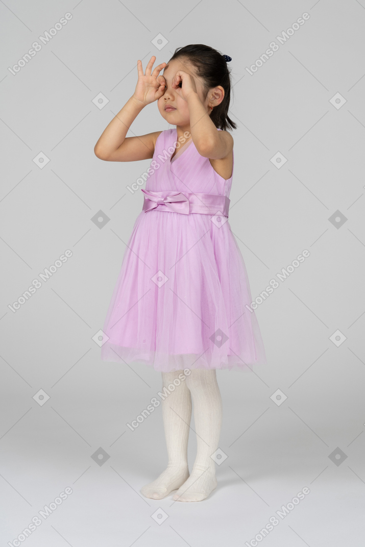Little girl in pink dress looking through finger mask