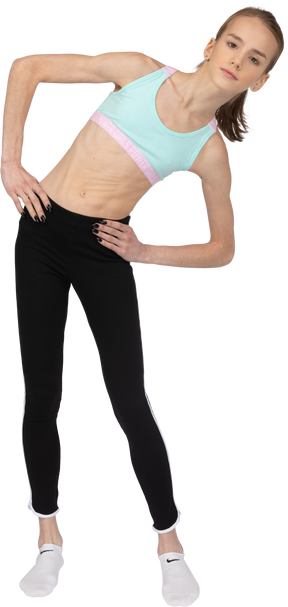 Vue de face d'une adolescente en tenue de sport mettant les mains sur les hanches tout en se penchant à droite