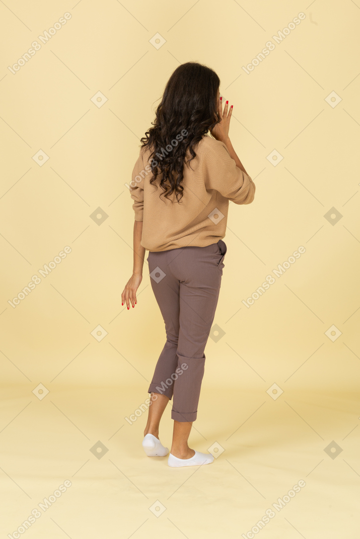 Three-quarter back view of a dark-skinned young female touching her ear