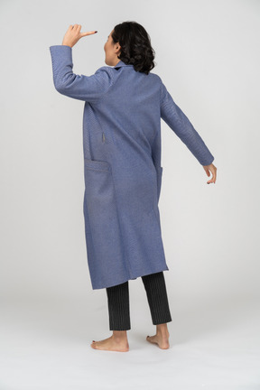 Вид сзади женщины в пальто, указывающей пальцем