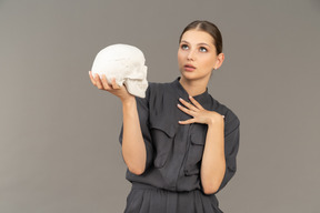 Vue de face d'une jeune femme en combinaison tenant un crâne en plâtre