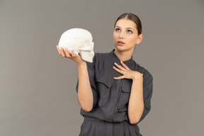 Front view of a young woman in a jumpsuit holding a plaster skull