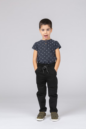 Vista frontal de un chico lindo de pie con las manos en los bolsillos y mirando a la cámara