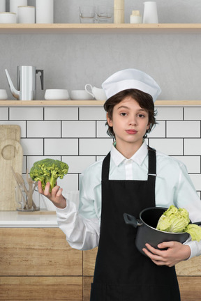 A boy in a chef's outfit holding a piece of broccoli