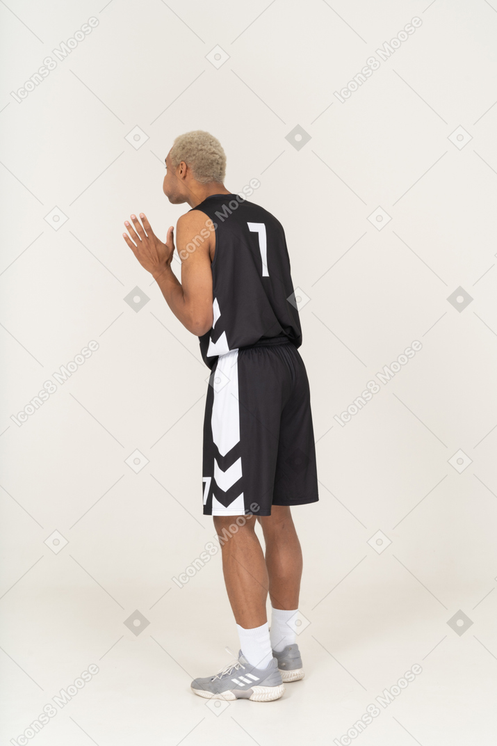 Dreiviertelansicht eines jungen männlichen basketballspielers, der wangen bläst und die hände hebt