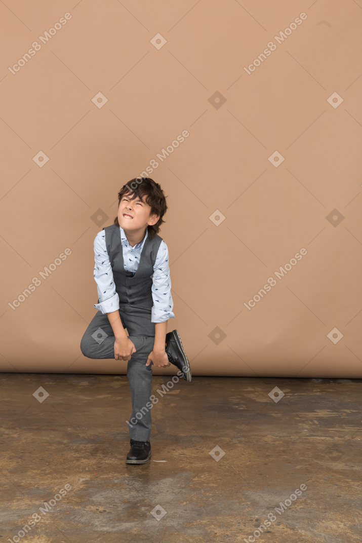 Vue de face d'un garçon en costume debout sur une jambe et faisant des grimaces