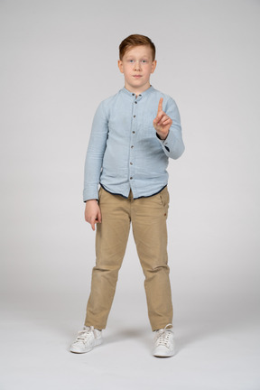 Vista frontal de un niño apuntando hacia arriba con el dedo y mirando a la cámara