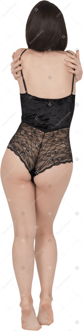 Unrecognizable female in black lace bodysuit embracing herself back to camera