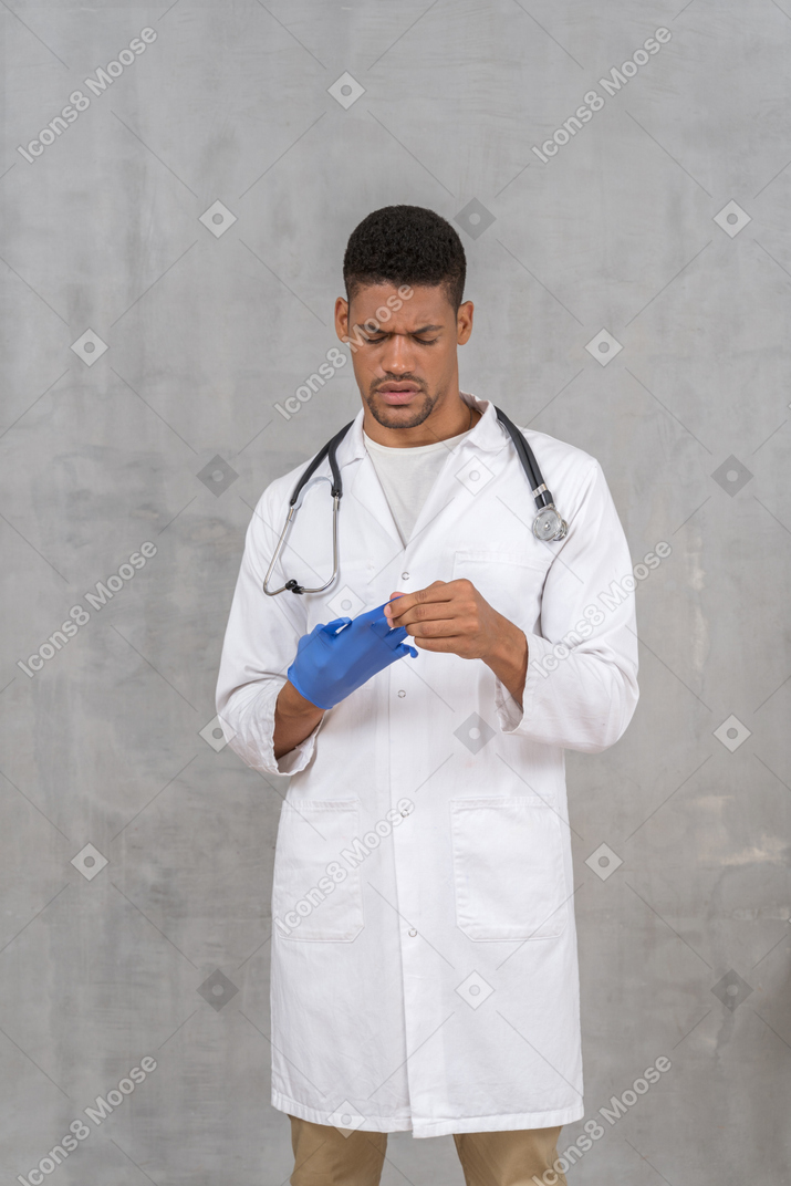 Young male doctor taking off his gloves