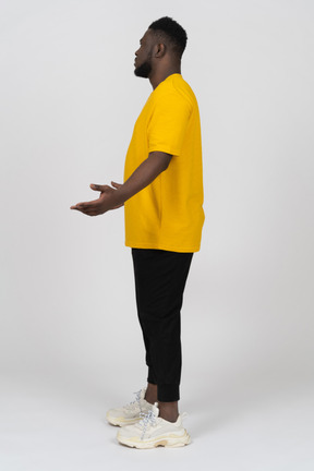 Side view of a displeased young dark-skinned man in yellow t-shirt outspreading hands