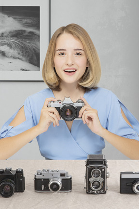 Smiling young woman sitting with retro cameras on the table