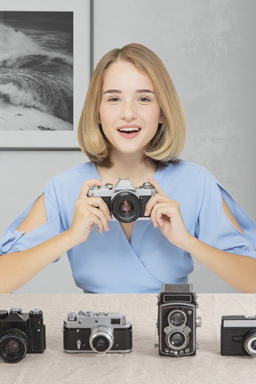 Mujer joven sonriente sentada con cámaras retro en la mesa