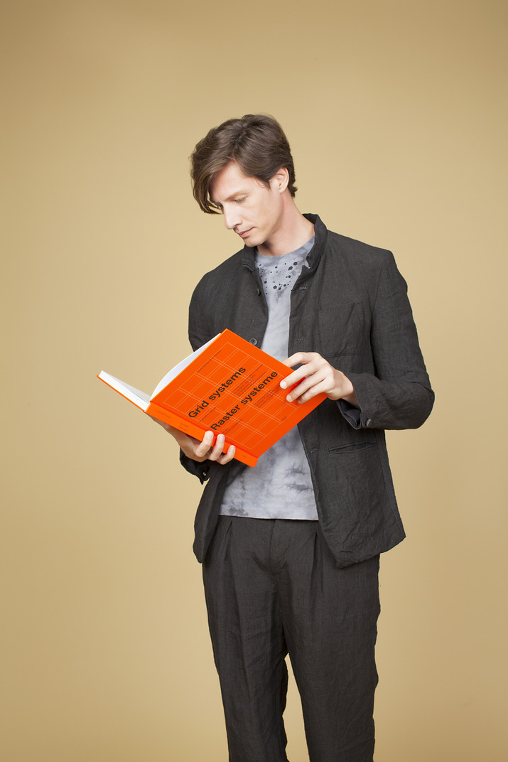 Young man holding an orange book and looking somewhere