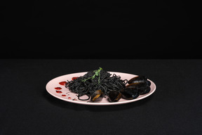 Black pasta with mussels on pink plate in black background