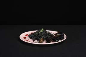 Pasta nera con cozze sul piatto rosa in sfondo nero