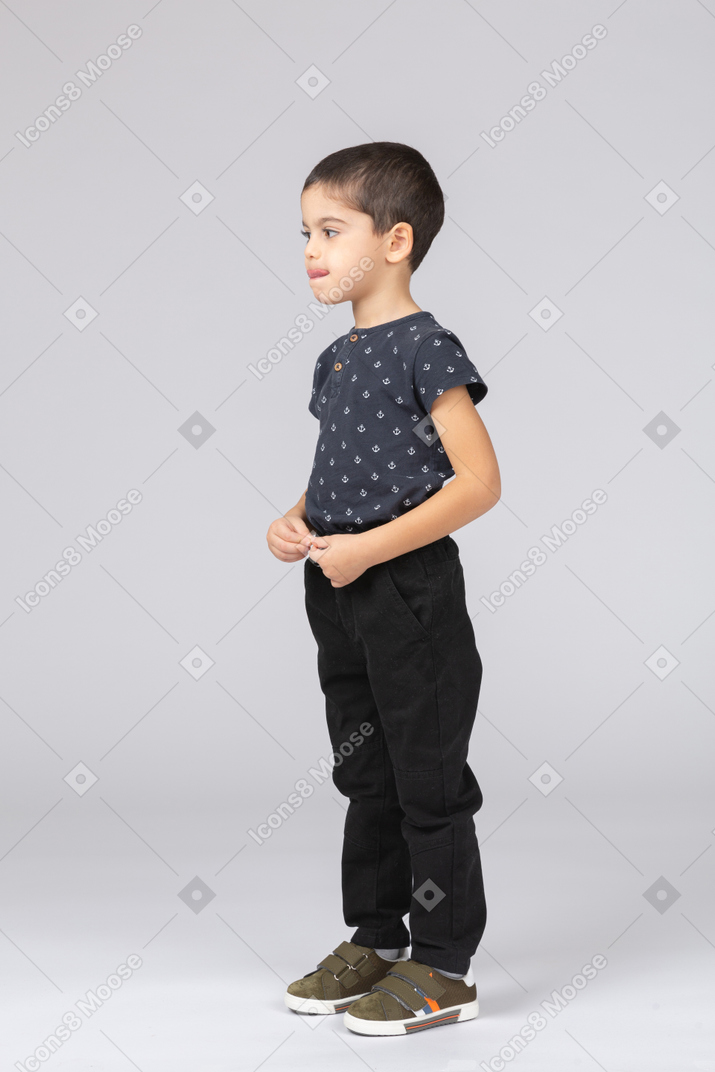 Cute kid boy in casual clothes standing in profile and making faces