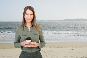 A woman standing on a beach holding a coffee cup