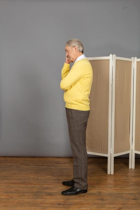 Side view of a thoughtful old man touching chin near the screen