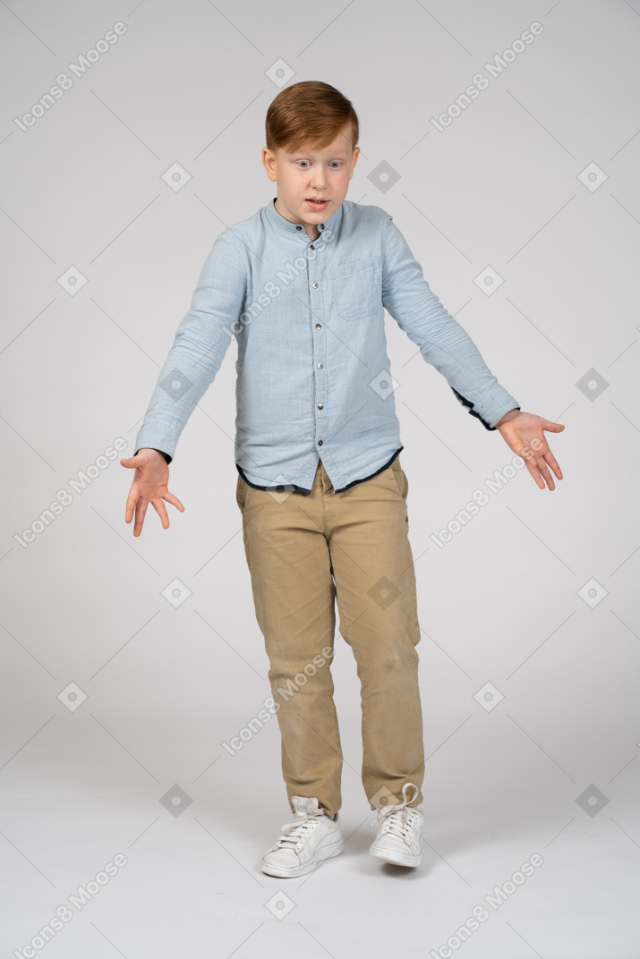 Front view of a confused boy standing with outstretched arms