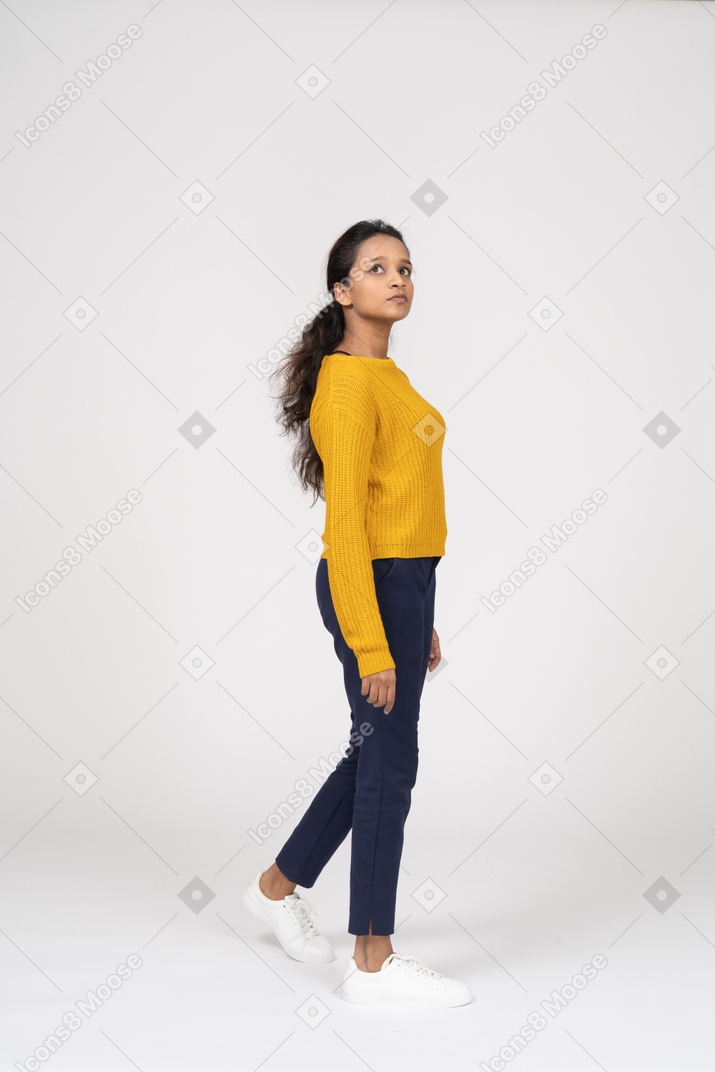 Vista lateral de una niña en ropa casual caminando y mirando hacia arriba