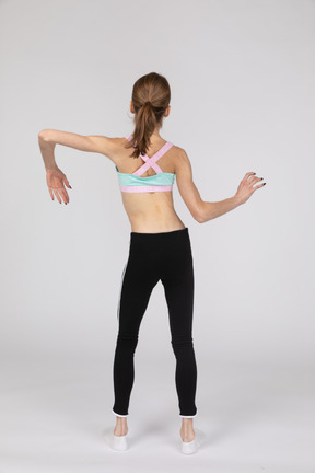 Vista posterior de una jovencita en ropa deportiva inclinando los hombros y haciendo olas