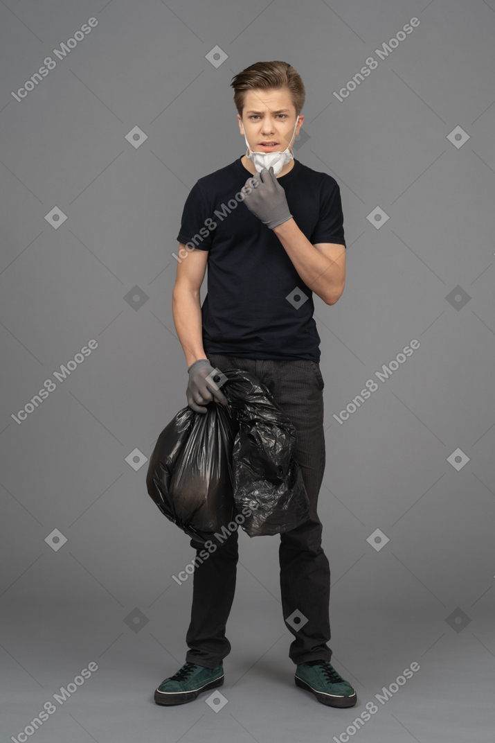 Unsatisfied young man looking at camera with a trash bag in his hands