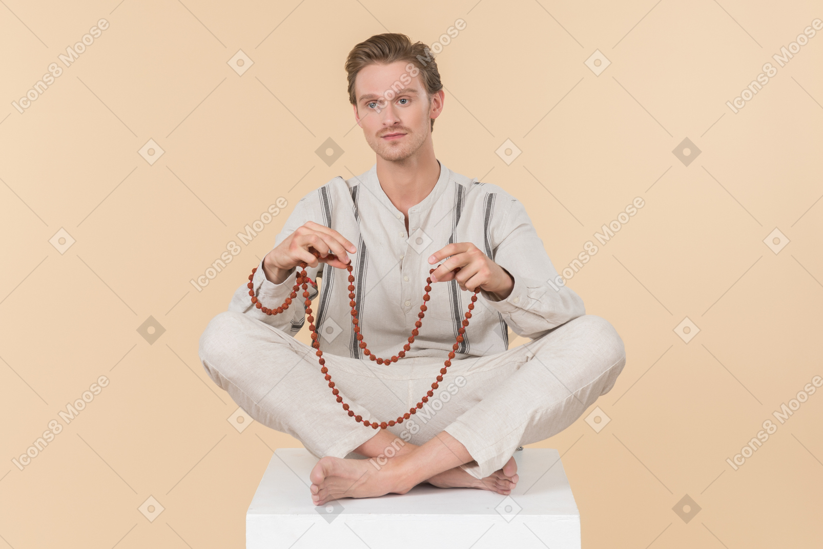 Young caucasian man sitting in lotus position and holding a necklace