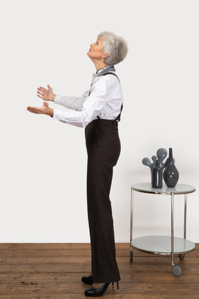 Vista lateral de una anciana extendiendo sus manos mientras mira hacia arriba
