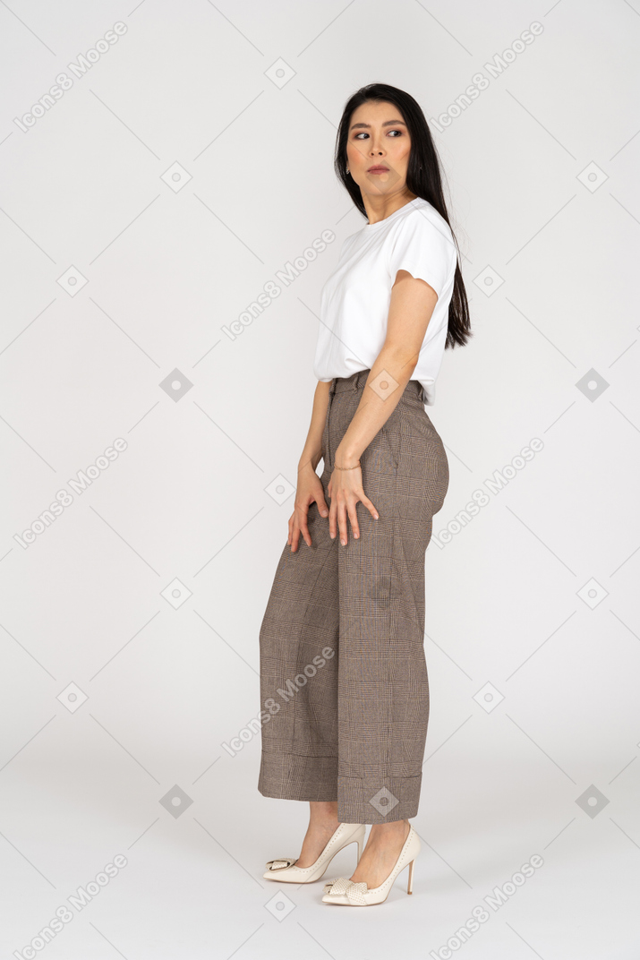 Vista laterale di una giovane donna sospettosa in calzoni e maglietta che osserva da parte