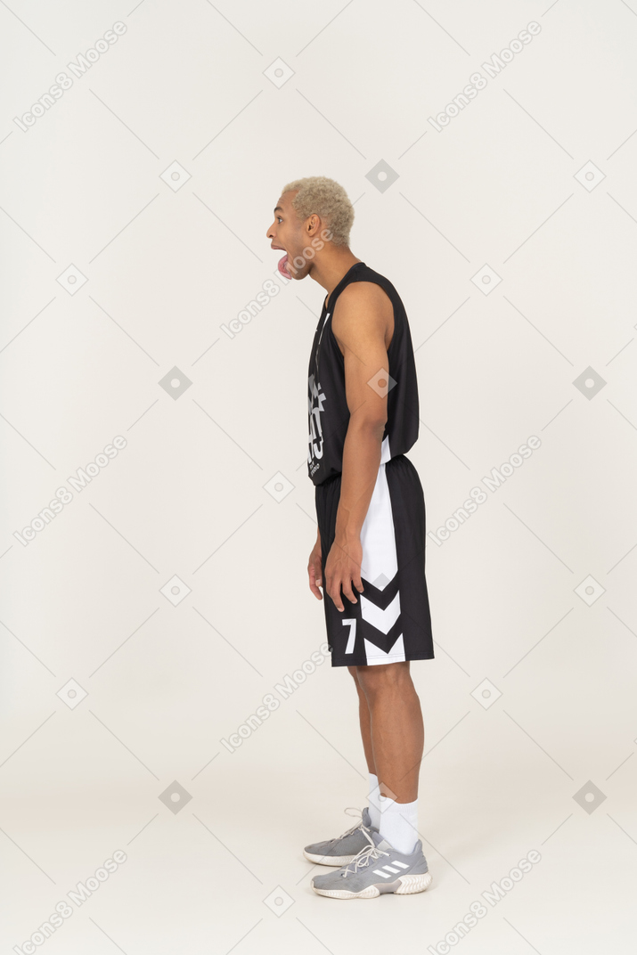 Vista lateral de um jovem louco jogador de basquete mostrando a língua