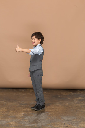 Vista lateral de un niño con traje gris que muestra el pulgar hacia arriba