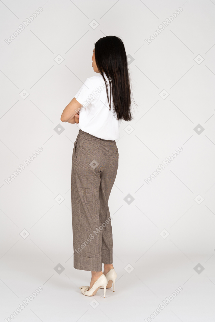 Three-quarter back view of a pouting young lady in breeches and t-shirt crossing hands