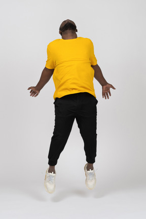 Vorderansicht eines springenden jungen dunkelhäutigen mannes in gelbem t-shirt mit ausgebreiteten händen