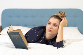Front view of a young female reading book in bed