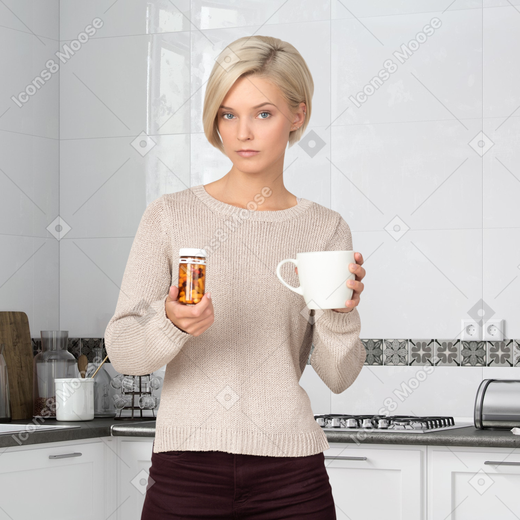A woman holding a pill bottle and a cup of tea