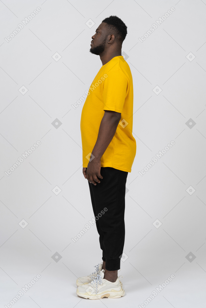 一个身穿黄色 t 恤、站着不动的黑皮肤年轻男子的侧视图