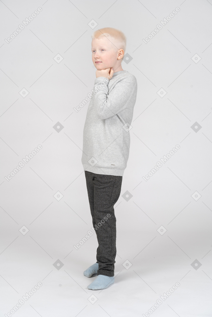 Front view of a thoughtful kid boy touching chin and looking aside