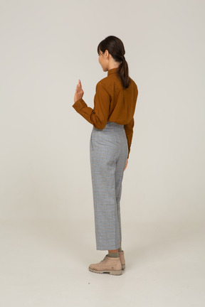 一位身着马裤和衬衫的年轻亚洲女性的四分之三后视图，显示出 ok 的手势