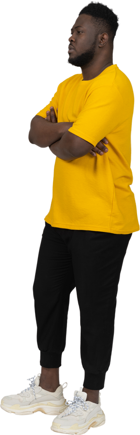 Three-quarter view of a young dark-skinned man in yellow t-shirt crossing arms