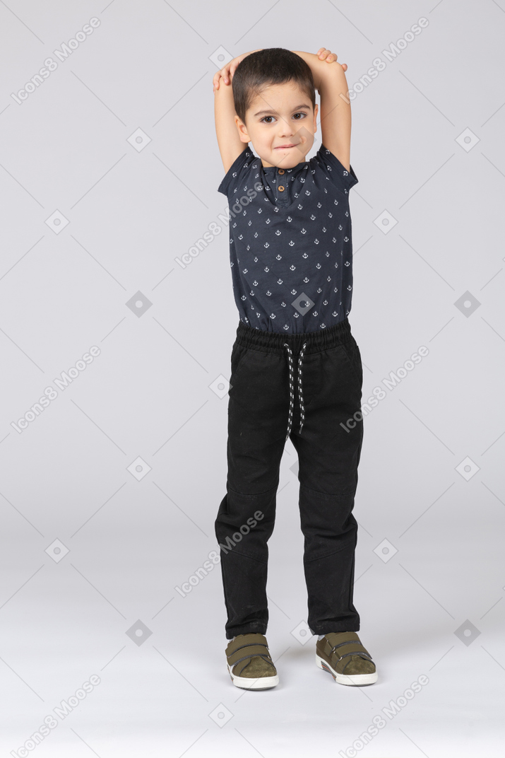 Front view of a cute boy standing with hands above head and looking at camera