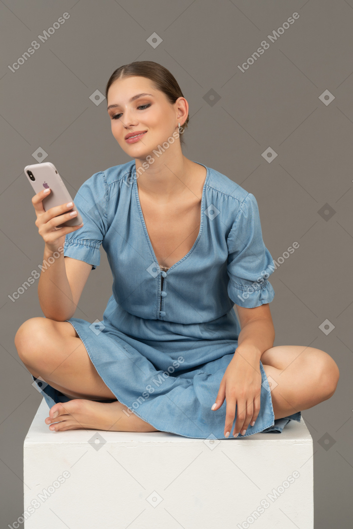 Vista frontale della giovane donna seduta su un cubo e messaggistica telefonica