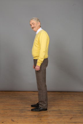 Seitenansicht eines alten fröhlichen mannes im gelben pullover, der lächelt und kamera betrachtet