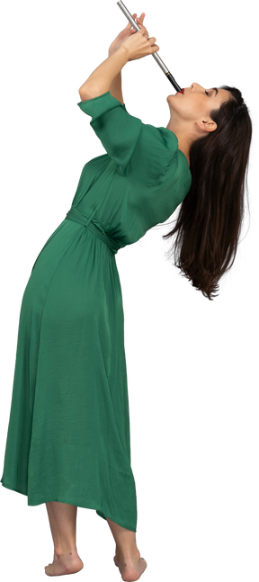 Vista lateral de una señorita en vestido verde tocando la flauta mientras se inclina hacia atrás