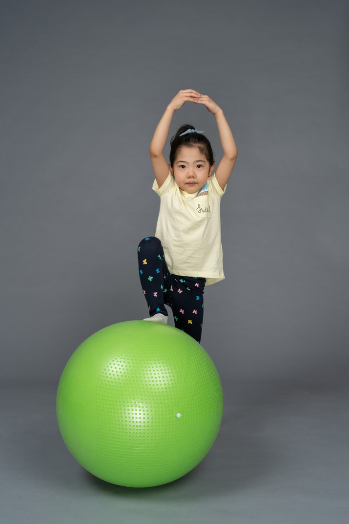 Little girl stepping on a green fitball with her hands above head