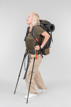 Smiling mature female tourist carrying backpack and walking with walking sticks