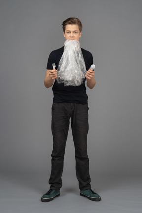 Male model holding plastic fork and spoon with plastic wrap in his mouth