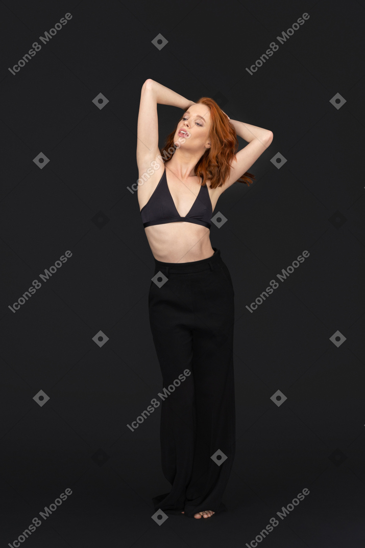A frontal view of the sexy young woman standing on the black background looking to the left