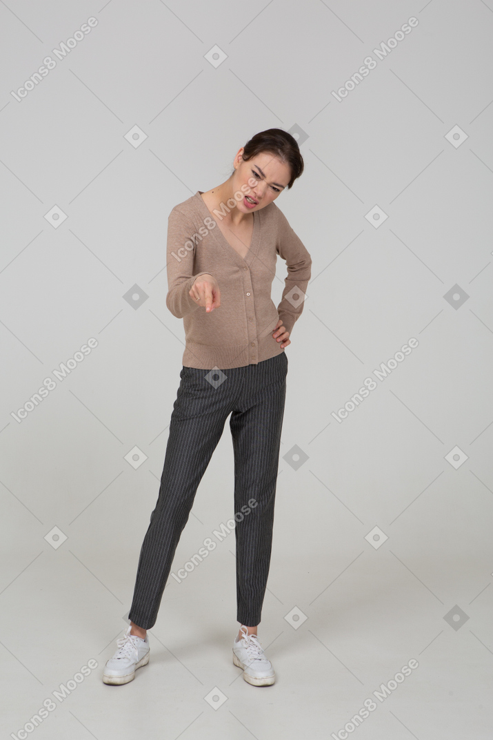 Front view of a furious young lady in beige pullover pointing finger